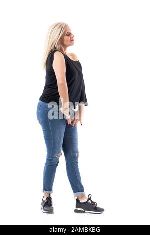 Vue latérale d'une femme réfléchie et décontractée du milieu de l'âge se posant et regardant vers le bas. Longueur totale du corps isolée sur fond blanc. Banque D'Images