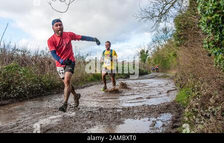 Les coureurs de compétition, hommes et femmes, se courbent dans des flaques boueuses Une voie de campagne lors d'une journée d'hiver ensoleillée en janvier Au Royaume-Uni Banque D'Images