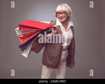 Shopper senior femme tenant des sacs de shopping posing heureux sourire et excité Banque D'Images