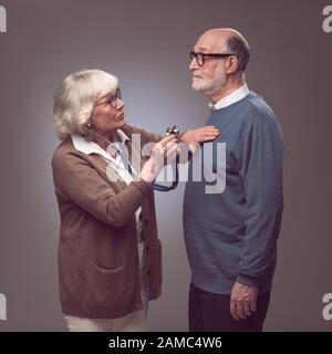 Femme senior prenant soin du mari, en vérifiant le rythme cardiaque avec stéthoscope Banque D'Images