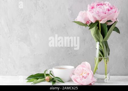 Bouquet de fleurs de pivoine rose festive avec tasse à café sur table blanche avec espace de copie. Toujours la vie. Jour ou fond de mariage pour femme Banque D'Images