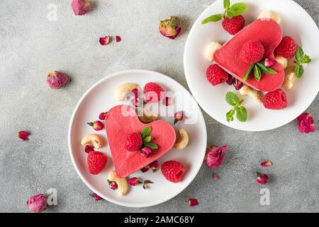 Dessert de Saint Valentin. Gâteaux rouges de légumes crus en forme de coeur avec framboises, fleurs de roses séchées et menthe. Nourriture saine et délicieuse. Vue de dessus. Concept d'amour Banque D'Images