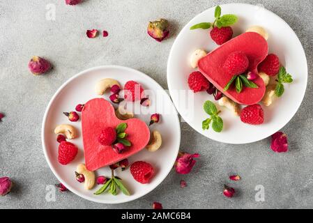 gâteaux faits maison en forme de coeur de végétalien avec framboises fraîches, menthe, fleurs de roses séchées et noix de cajou. dessert de saint valentin. concept de cuisine végétalienne saine. Banque D'Images