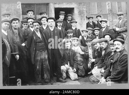 Les travailleurs, la structure sociale. Gaffer, patron, casquette, patron. Victorian groupe de travailleurs dans des vêtements de travail traditionnel à l'extérieur d'une usine. Banque D'Images