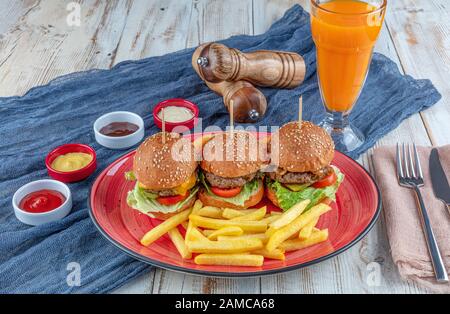 Trois mini hamburgers. Délicieux trois mini-hamburgers maison servis avec salade, sauce et rondelles d'oignon et frites. Mini-hamburgers faits maison. Banque D'Images
