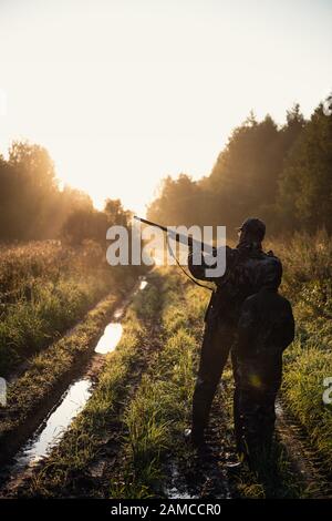 Chasseurs avec équipement de chasse allant à travers le champ rural vers la forêt au coucher du soleil pendant la saison de chasse dans la campagne Banque D'Images