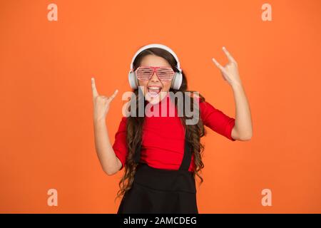 Accessoire de fête. Amuse-toi bien. Liste de lecture pour la fête. Concept de musique. Enfant porter des lunettes. Magasin de mode de lunettes. Piste froide. Fille avec lunettes arrière-plan orange. Événement et divertissement. Fille de fête. Banque D'Images