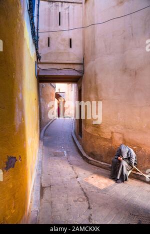 Un vieux mendiant dans une rue vide dans la médina de Fes, Maroc. Banque D'Images