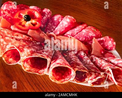 Délicieux apéritif pour les vacances. Plaque avec des tranches de jamon et de salami émincées, roulée et décorée d'une tranche de laitue rouge et de grenade Banque D'Images