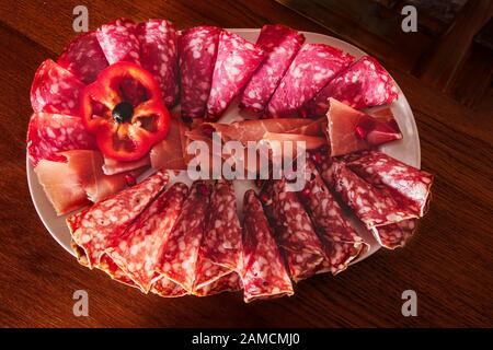 Délicieux apéritif pour les vacances. Plaque avec des tranches de jamon et de salami émincées, roulée et décorée d'une tranche de laitue rouge et de grenade Banque D'Images