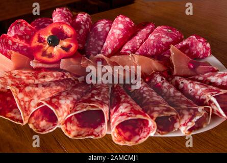 Délicieux apéritif pour les vacances. Plaque avec des tranches de jamon et de salami émincées, roulée et décorée d'une tranche de laitue rouge et de grenade Banque D'Images