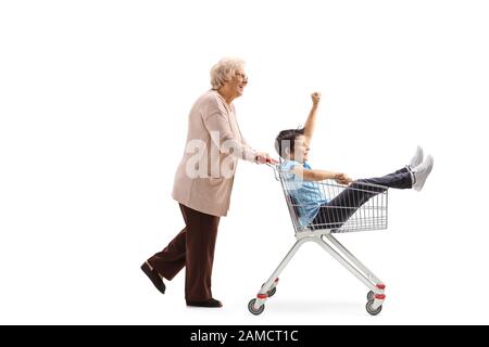 Photo pleine longueur d'une grand-mère poussant un panier avec un garçon assis à l'intérieur isolé sur fond blanc Banque D'Images