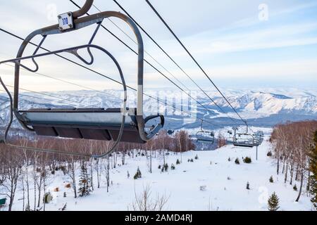 Un télésiège à télécabine avec cabine suspendue sur un câble dans lequel se trouvent des personnes avec skis et snowboards sur un fond de montagnes, arbres avec sno Banque D'Images