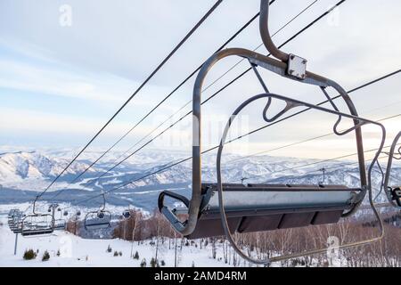 Un télésiège à télécabine avec cabine suspendue sur un câble dans lequel se trouvent des personnes avec skis et snowboards sur un fond de montagnes, arbres avec sno Banque D'Images
