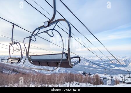 Un télésiège à télécabine avec cabine suspendue sur un câble dans lequel se trouvent des personnes avec skis et snowboards sur un fond de montagnes, arbres avec sno Banque D'Images