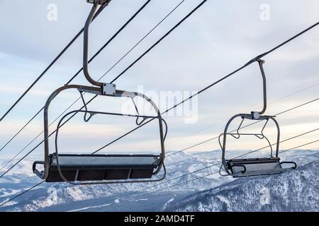 Un télésiège à télécabine avec cabine suspendue sur un câble dans lequel se trouvent des personnes avec skis et snowboards sur un fond de montagnes, arbres avec sno Banque D'Images