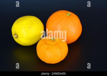 Fruits frais et lumineux, un citron jaune, un petit mandarine orange, un grand minéralola se trouve sur un fond en plastique noir. Banque D'Images