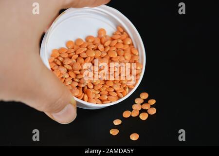 Grains, graines de lentilles rouges, une poignée de lentilles sont situées et dispersées dans une couverture en plastique blanc sur fond en plastique noir. Banque D'Images