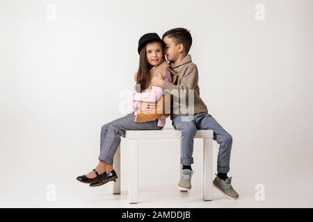 Joli petit couple fille et garçon élégant dans des vêtements tendance qui s'embrassaient ensemble en studio. Enfant garçon épouse une fille et lui raconte une histoire drôle. Enfants fash Banque D'Images