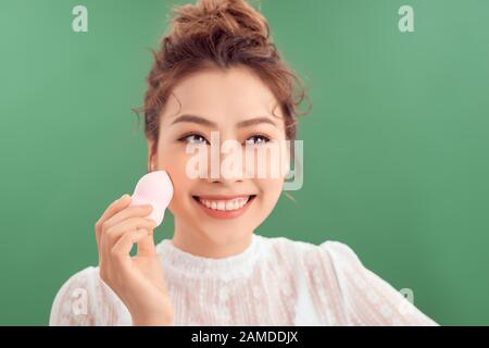 Portrait de beauté d'une jeune vietnamienne souriante magnifique isolée sur fond vert, tenant éponge de maquillage Banque D'Images