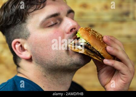 Le jeune homme mange un délicieux hamburger appétissant. Banque D'Images