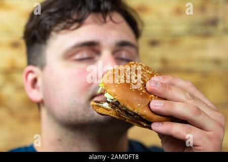 Le jeune homme mange un délicieux hamburger appétissant. Banque D'Images