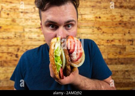 Un jeune homme se pose avec son délicieux hamburger et est sur le point de l'apprécier. Banque D'Images