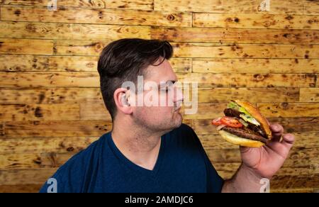 Un jeune homme se pose avec son délicieux hamburger et est sur le point de l'apprécier. Banque D'Images