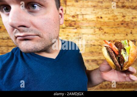 Un jeune homme se pose avec son délicieux hamburger et est sur le point de l'apprécier. Banque D'Images