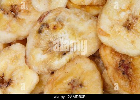 Chips de banane déshydratée, tranches de bananes mûres fraîches comme arrière-plan de l'alimentation. Banque D'Images