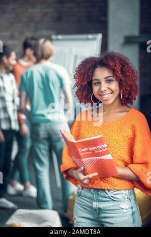 Un élève joyeux aux cheveux rouges se sentant joyeux tout en étudiant avec des amis Banque D'Images