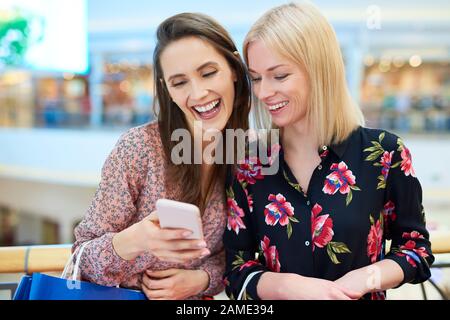Joyeux amis utilisant le téléphone mobile pendant les achats dans le centre commercial Banque D'Images