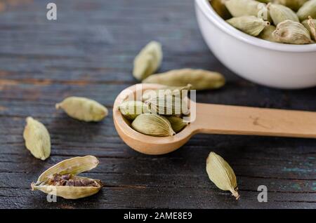 Gousses de cardamome vert séché dans un bol sur table en bois, ferme et vue de dessus. Banque D'Images