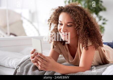 Belle femme utilisant un smartphone dans le lit Banque D'Images