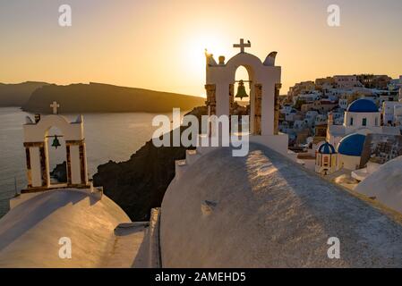 Églises à dôme bleu et clocher face à la mer Égée avec lumière chaude au coucher du soleil à Oia, Santorin, Grèce Banque D'Images