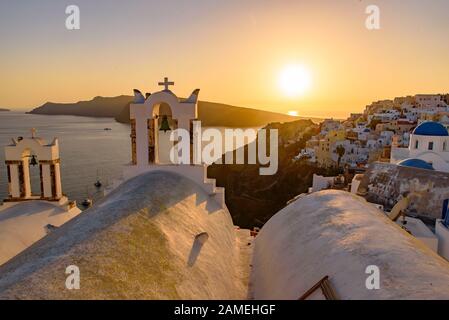 Églises à dôme bleu et clocher face à la mer Égée avec lumière chaude au coucher du soleil à Oia, Santorin, Grèce Banque D'Images