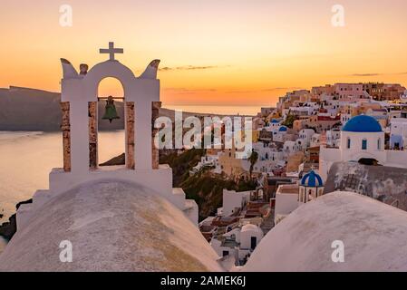 Églises à dôme bleu et clocher face à la mer Égée avec lumière chaude au coucher du soleil à Oia, Santorin, Grèce Banque D'Images