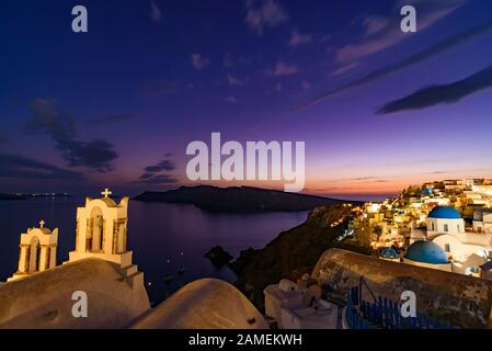 Églises à dôme bleu et clocher face à la mer Égée avec lumière chaude au coucher du soleil à Oia, Santorin, Grèce Banque D'Images