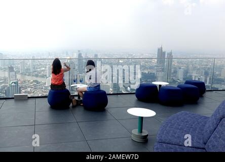 Deux femmes assises sur le toit de King Power MahaNakhon bâtiment avec un verre bleu sur la table et regarder la ville de Bangkok. Banque D'Images