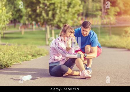 Une femme de sport se blessant pendant le jogging dans le parc et aidée par un entraîneur masculin Banque D'Images