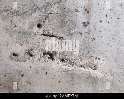 Surface en béton avec cavernes et pierres de gravier exposées et barres de renfort. Banque D'Images