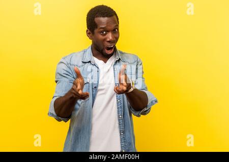 Portrait de criminel de rue, dangereux jeune homme dans denim décontracté chemise pointant avec des pistolets à doigt, debout avec une bouche ouverte et menaçant de tirer Banque D'Images