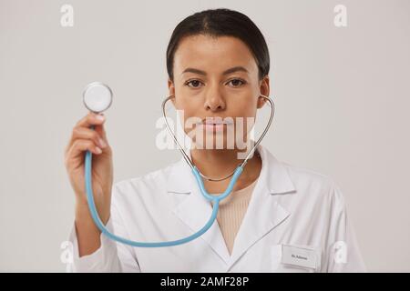 Tête et épaules portrait de belle femme médecin tenant stéthoscope et regardant l'appareil photo tout en se tenant sur fond blanc, espace de copie Banque D'Images