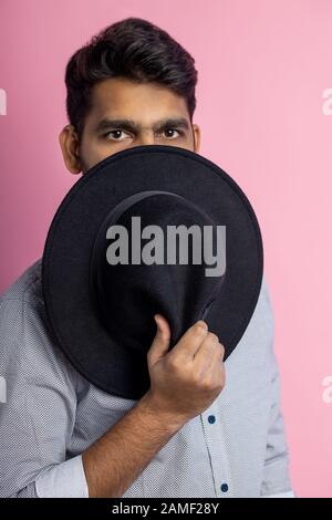 Gros plan vertical de jeune homme avec peau brune, sourcils broussailleux, coiffure élégante, regard perceptible, couvrant la moitié du visage avec chapeau noir, fatigué Banque D'Images