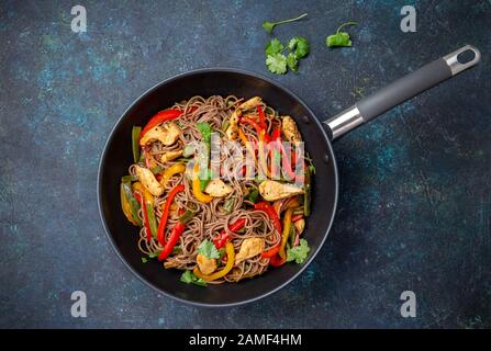 Nouilles soba sarrasin plat japonais avec le poulet et les légumes la carotte, le poivron et les haricots verts dans le wok sur fond bleu foncé Banque D'Images