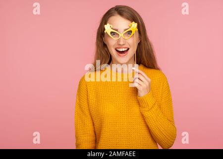 Portrait d'une jeune fille au gingembre drôle et joyeuse dans un pull décontracté portant de fausses lunettes en papier et regardant un appareil photo avec surprise, s'amuser, mas Banque D'Images