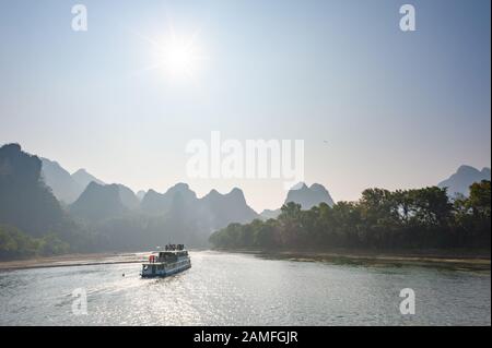 Bateau sur la rivière Li croisière contre le soleil et le karst formation paysage de montagne dans le brouillard entre Guiling et Yangshuo, province de Guangxi, Chine Banque D'Images