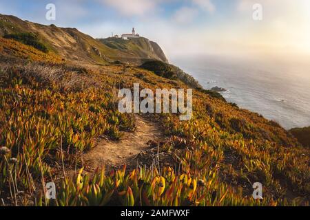 Sintra Portugal. Phare Sur Le Cap Roca. Chemin de voyage et de randonnée éclairé par un coucher de soleil doré. Site touristique avec de belles falaises de côte le long Banque D'Images