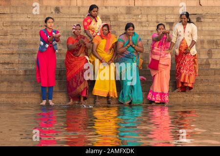 Varanasi, INDE, 18 JANVIER 2019 : un groupe de femmes portant des robes traditionnelles colorées prient avant de commencer un bain spirituel au lever du soleil le long Banque D'Images