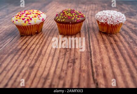 17 gros plan de trois cupcakes en ligne sur un fond en bois Uni avec espace de copie Banque D'Images